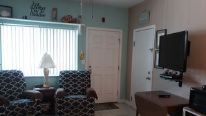 A living room with patterned armchairs, a coffee table, a television, and a door.