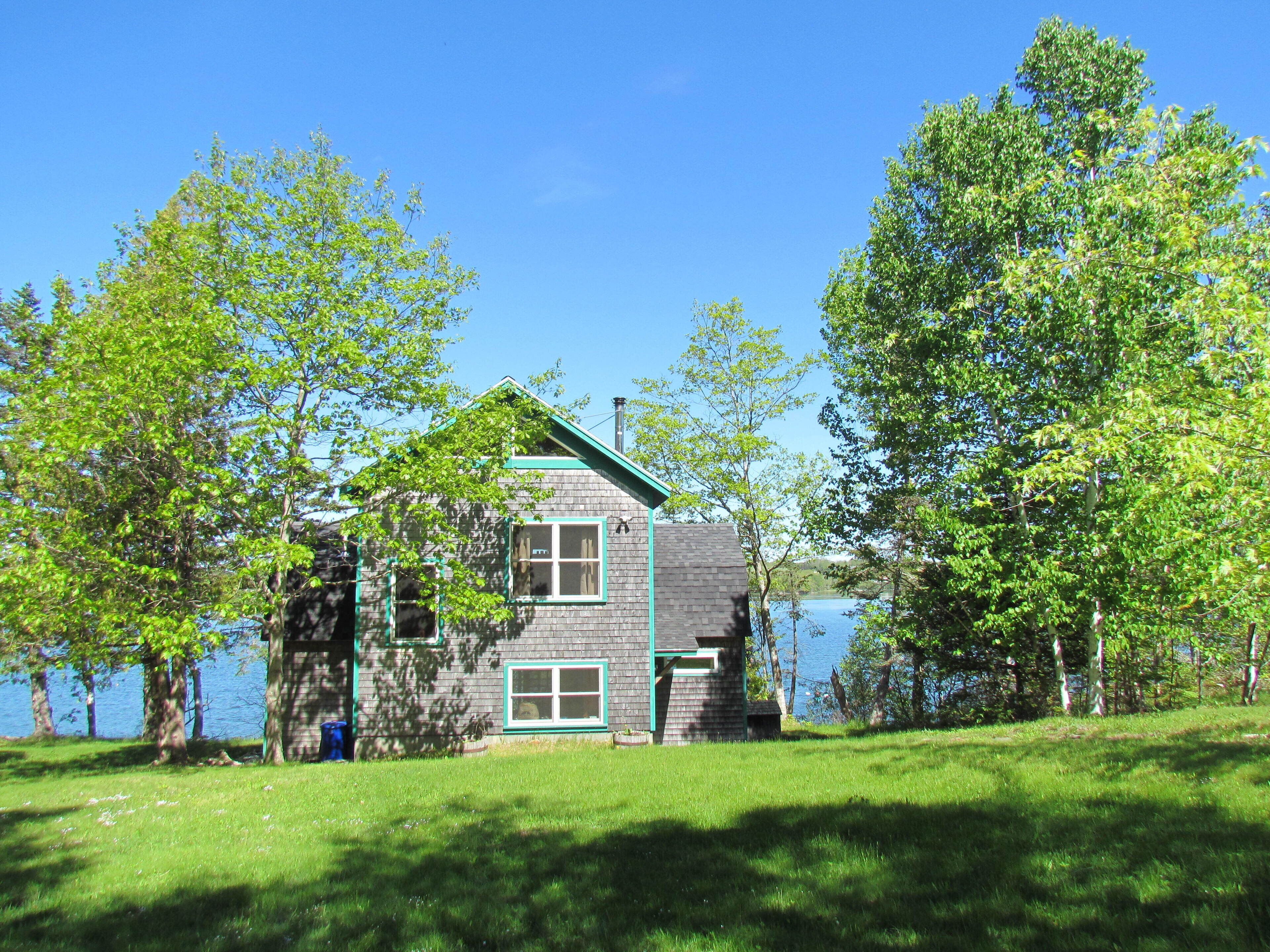 A two-story cabin with a green roof, surrounded by lush greenery and a lake.