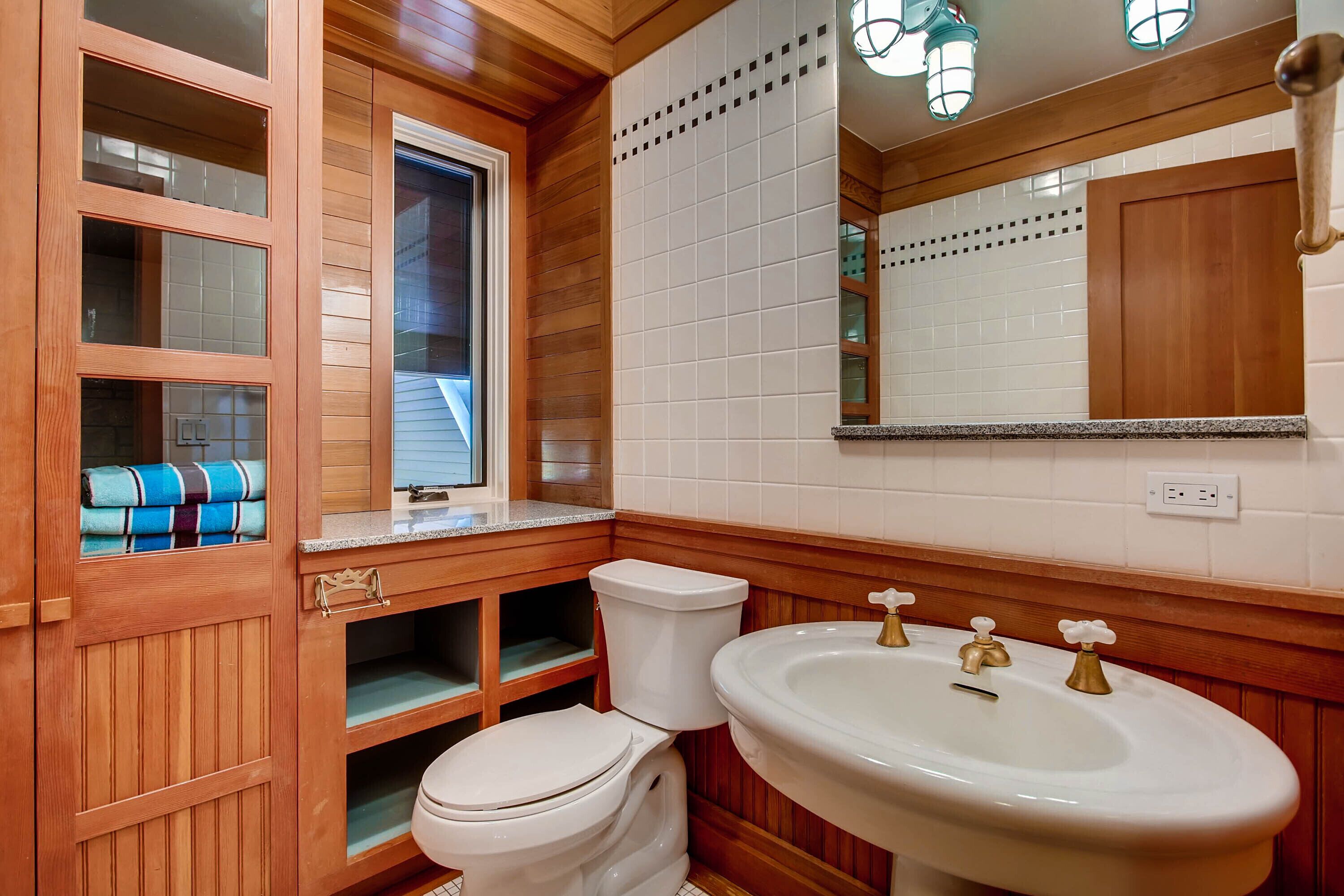 Un baño con paneles de madera, un inodoro, un lavabo y una ventana.