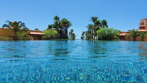 Una piscina blava cristal·lina envoltada de palmeres i un edifici d'hotel.