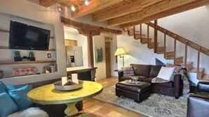 Un salon avec un canapé, une table basse, un téléviseur et un escalier.