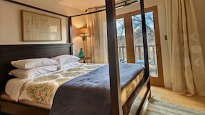 Un lit à baldaquin surmonté d’une couvre-lit à motifs, une œuvre d’art encadrée au-dessus, et une vue sur l’extérieur à travers une porte vitrée.