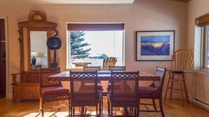 A dining area with a wooden table and chairs, a mirror, and a window with a view of a tree and mountains. - Single Level w/ Hot Tub and patios with 360° Views! (Westcliffe)