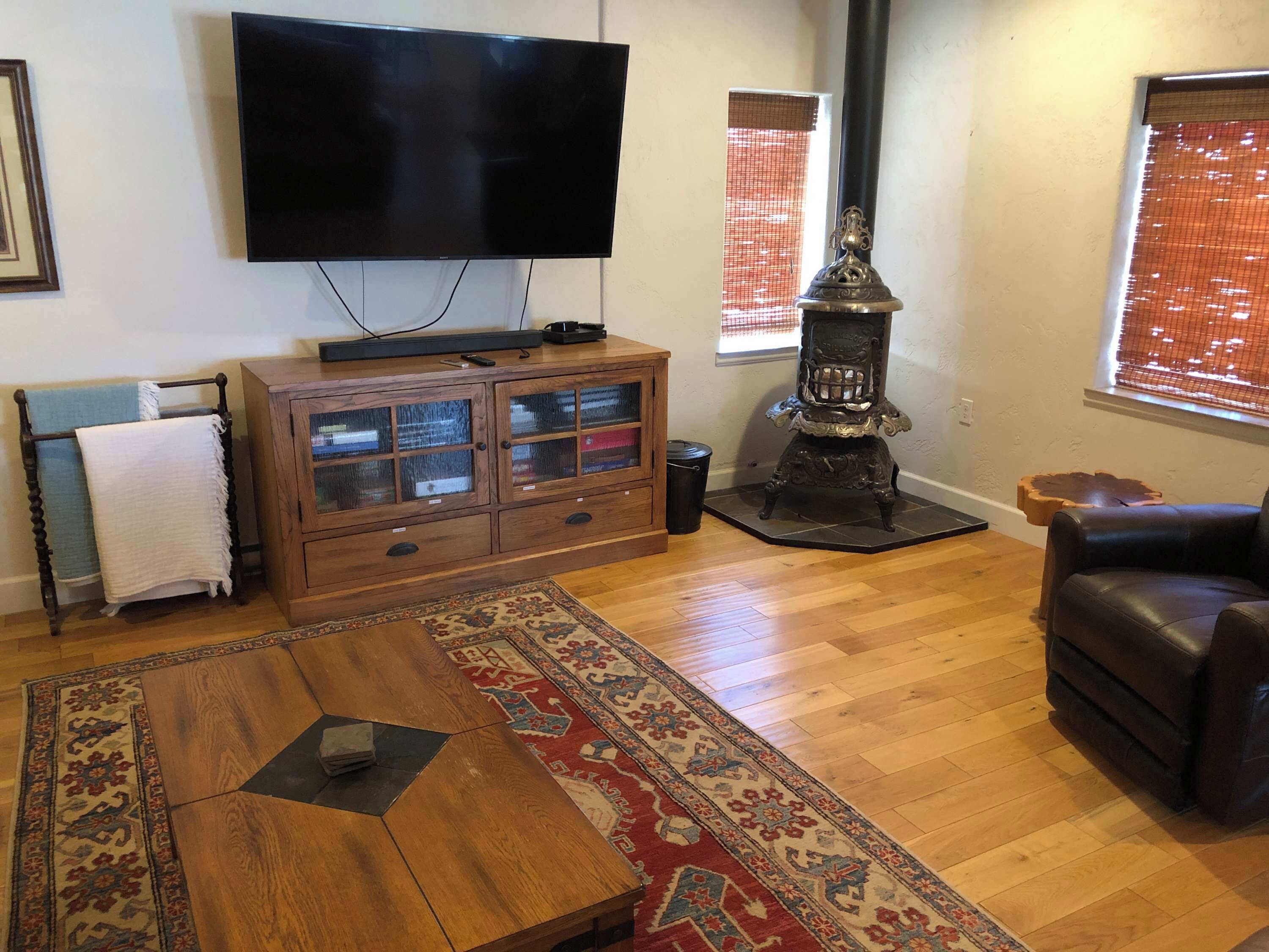 Ein Wohnzimmer mit Flachbildfernseher, Holzschrank, Teppich mit Muster und einer schwarzen Ledersofa.