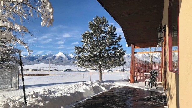 A snow-covered landscape with a wooden building, a tree, and mountains in the background. - Single Level w/ Hot Tub and patios with 360° Views! (Westcliffe)