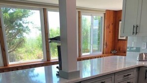 A modern kitchen with a built-in oven, white cabinets, and a large window offering a view of greenery outside. - 3 Br Cottage right on beach - Beautiful view of beach/water - Pets welcome! (Prime Hook Beach)