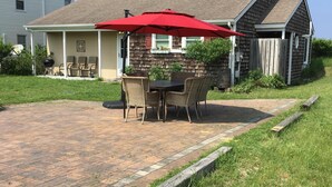 A patio with a brick floor, a table with chairs, and a red umbrella. - 3 Br Cottage right on beach - Beautiful view of beach/water - Pets welcome! (Prime Hook Beach)