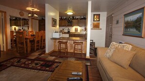 Una sala de estar acogedora con un sofá, una mesa de centro y un comedor con sillas de madera, con una cocina al fondo.