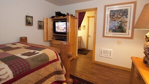 Una habitación acogedora con una cama de madera, un televisor en un mueble de madera y un cuadro en la pared.
