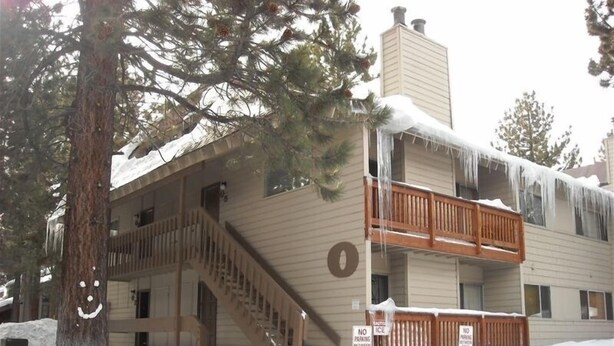 Un edificio de dos pisos con una escalera de madera que conduce a la entrada, rodeado de nieve.