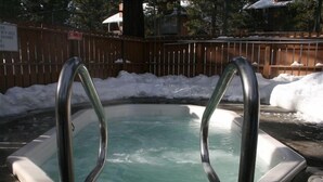 Un jacuzzi con escaleras metálicas, rodeado por una valla de madera y nieve.