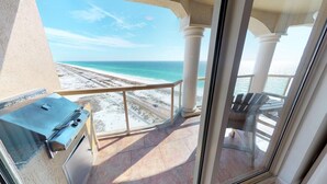 Un balcon avec vue sur la plage et l’océan, un barbecue et une chaise.