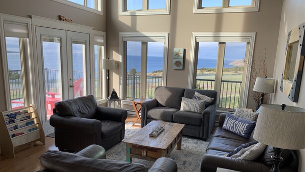 A spacious living room with leather sofas, a wooden coffee table, and a view of the ocean through large windows.