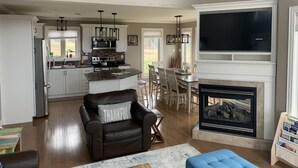A spacious living room with a fireplace, a dining area, and a kitchen with white cabinets and a large island.