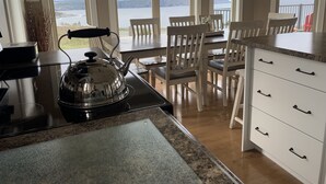 A kitchen with a view of a lake, a dining area with chairs, and a white cabinet with drawers.