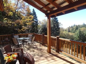 Une terrasse en bois, dotée de mobilier d’extérieur et offrant une vue sur une forêt.