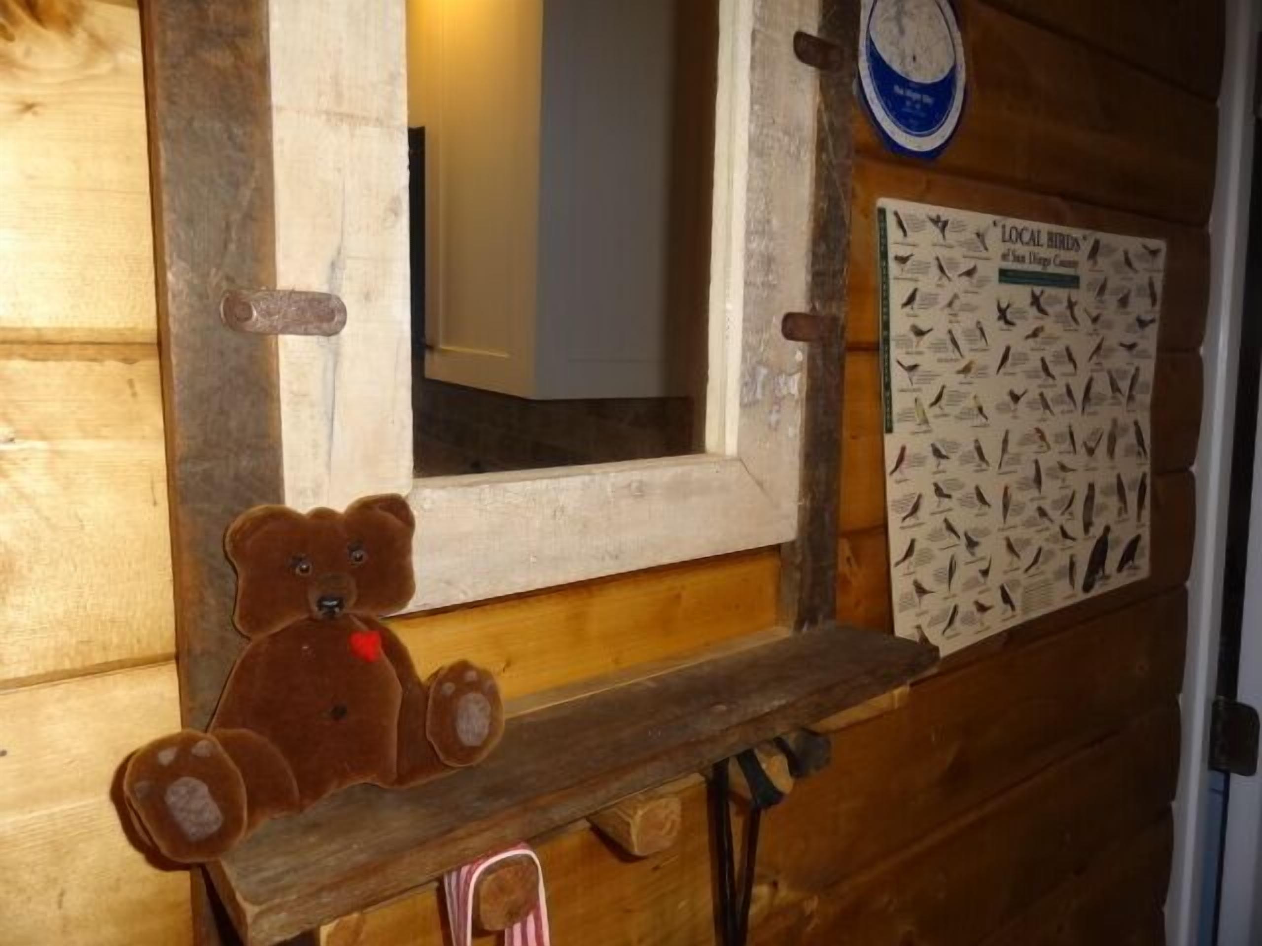 A wooden cabin interior with a mirror, a bear decoration, and a bird identification chart.