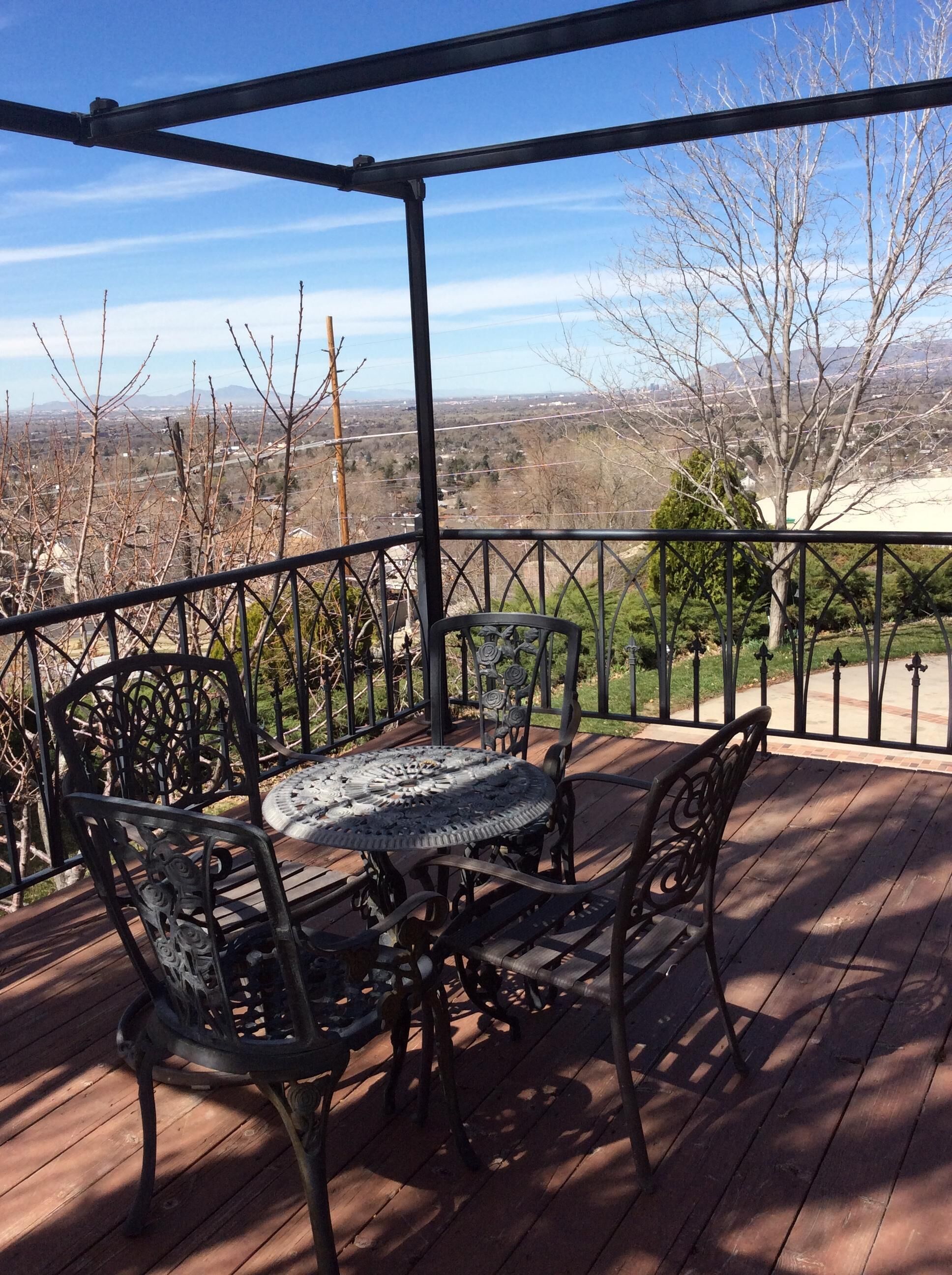 A covered outdoor patio with a table and chairs, overlooking a landscape with trees and distant buildings.