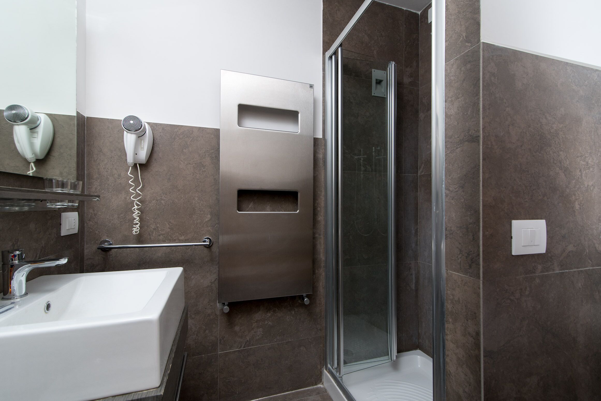 Ein modernes Badezimmer mit Waschbecken, Fön und Duschkabine.