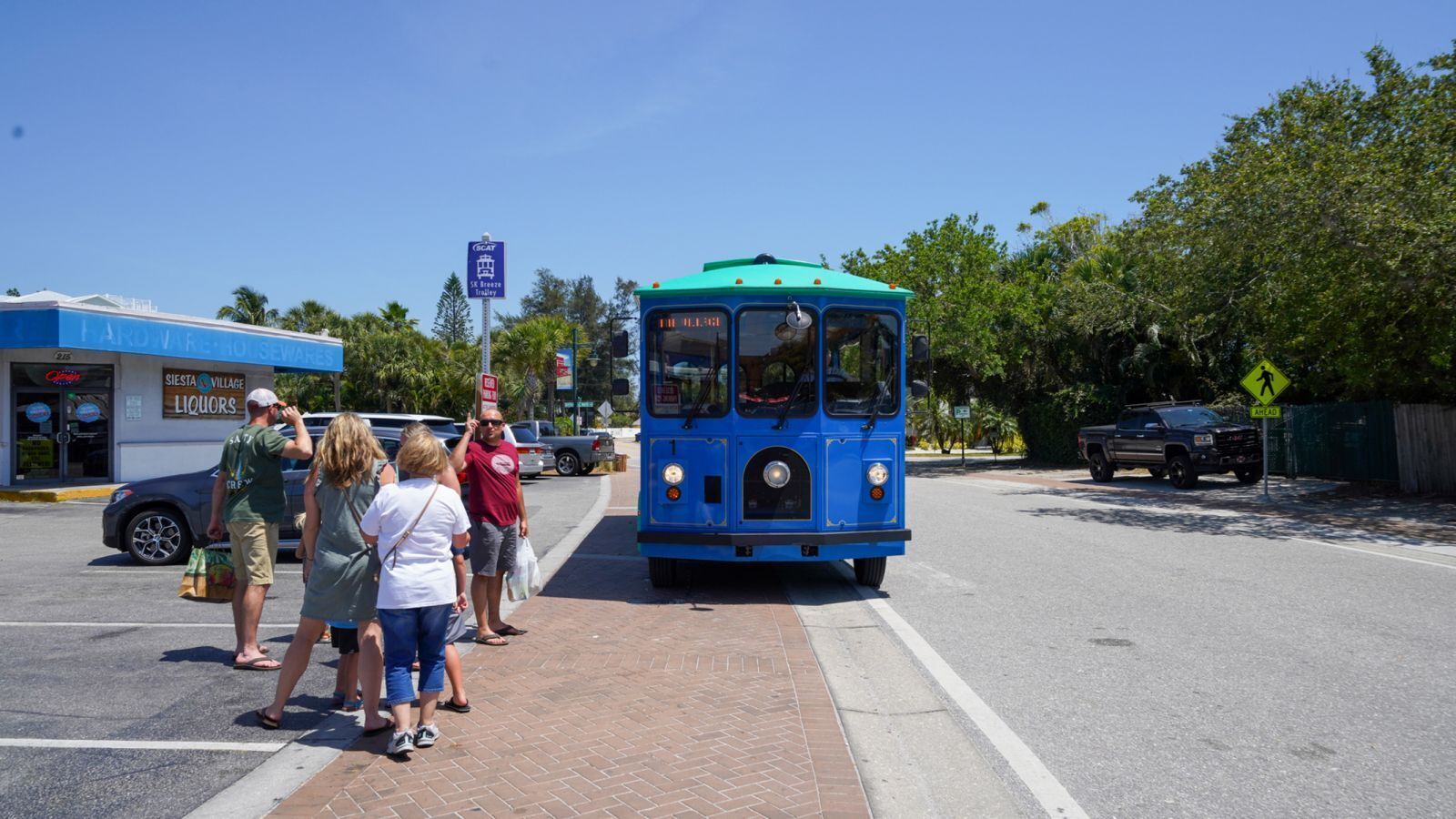 A blue trolley at a bus stop with people waiting.