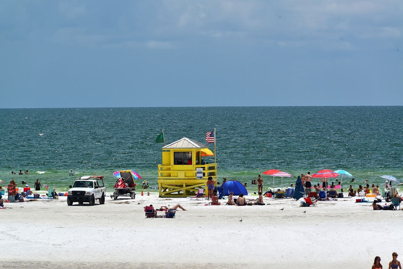 A beach with a lifeguard tower, umbrellas, and people relaxing.