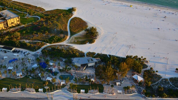 An aerial view of a beach resort with a large sandy beach, a parking area, and a building complex with multiple structures. -  🌷 Stunning 1-Bedroom Apartment Overlooking Pool, steps to Siesta Beach (Siesta Key)