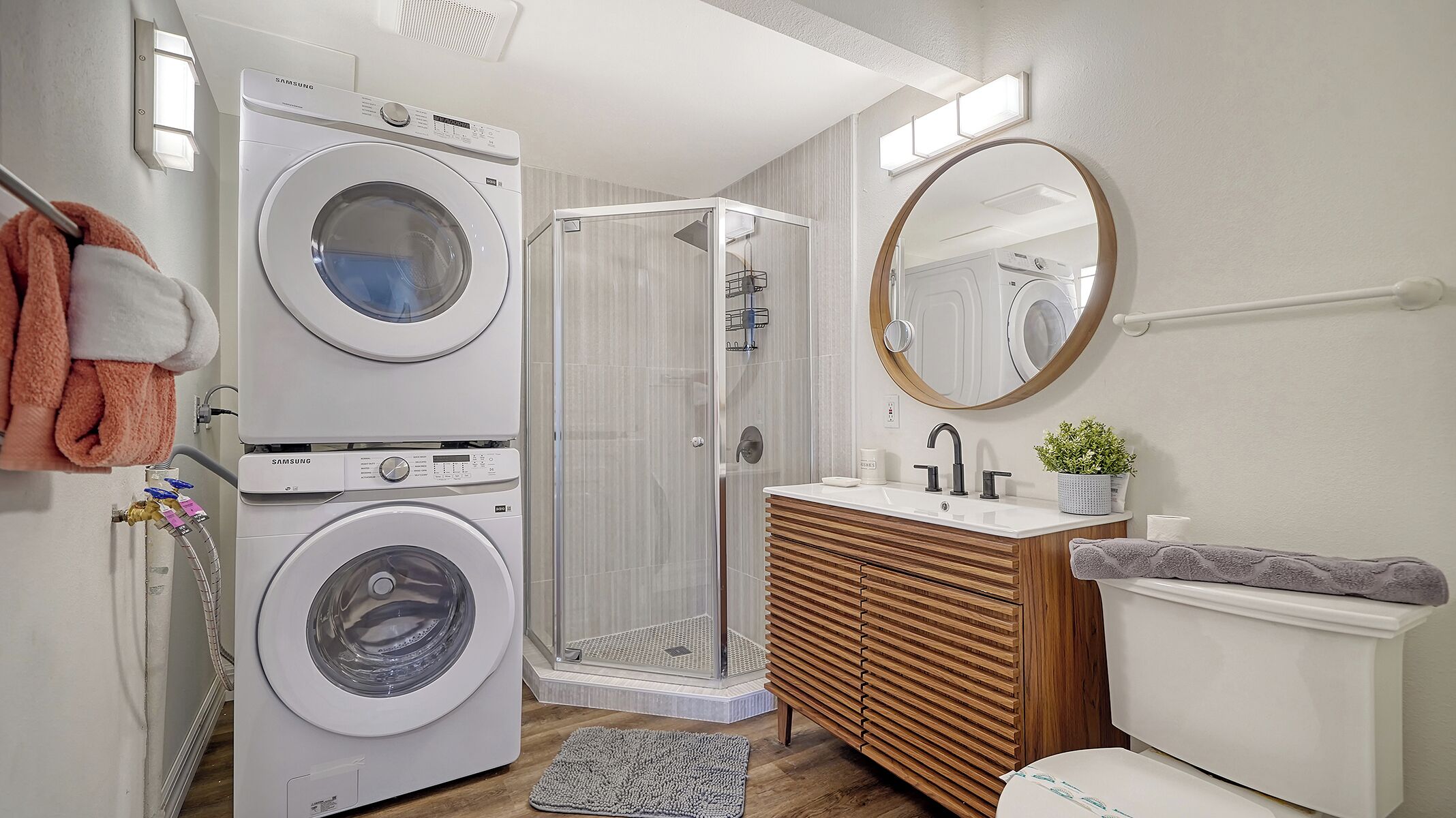 Une salle de bain moderne équipée d’un lave-linge, d’une cabine de douche et d’un meuble-lavabo avec un miroir.