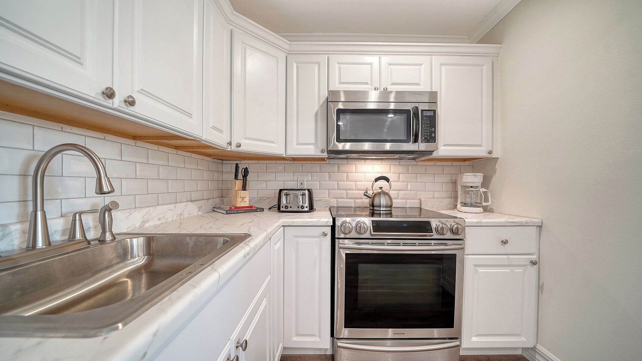 A compact kitchen with white cabinets, a stainless steel sink, a microwave, a toaster, and a coffee maker.