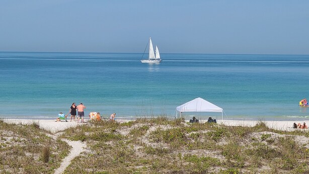 A beach with a sailboat, a tent, and people relaxing. - Beachfront Cottages GULF at Beautiful Sandy Shores on Gulf of America (Indian Rocks Beach)