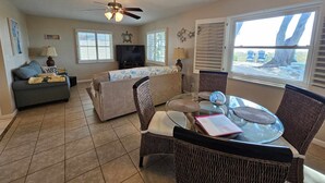 A living room with a ceiling fan, two sofas, a glass coffee table, wicker chairs, a TV, and a window with blinds. - Beachfront Cottages GULF at Beautiful Sandy Shores on Gulf of America (Indian Rocks Beach)