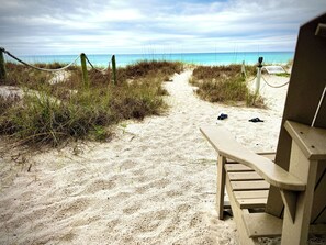 En sandig strandpromenad med en träbänk och ett avspärrningsrep.