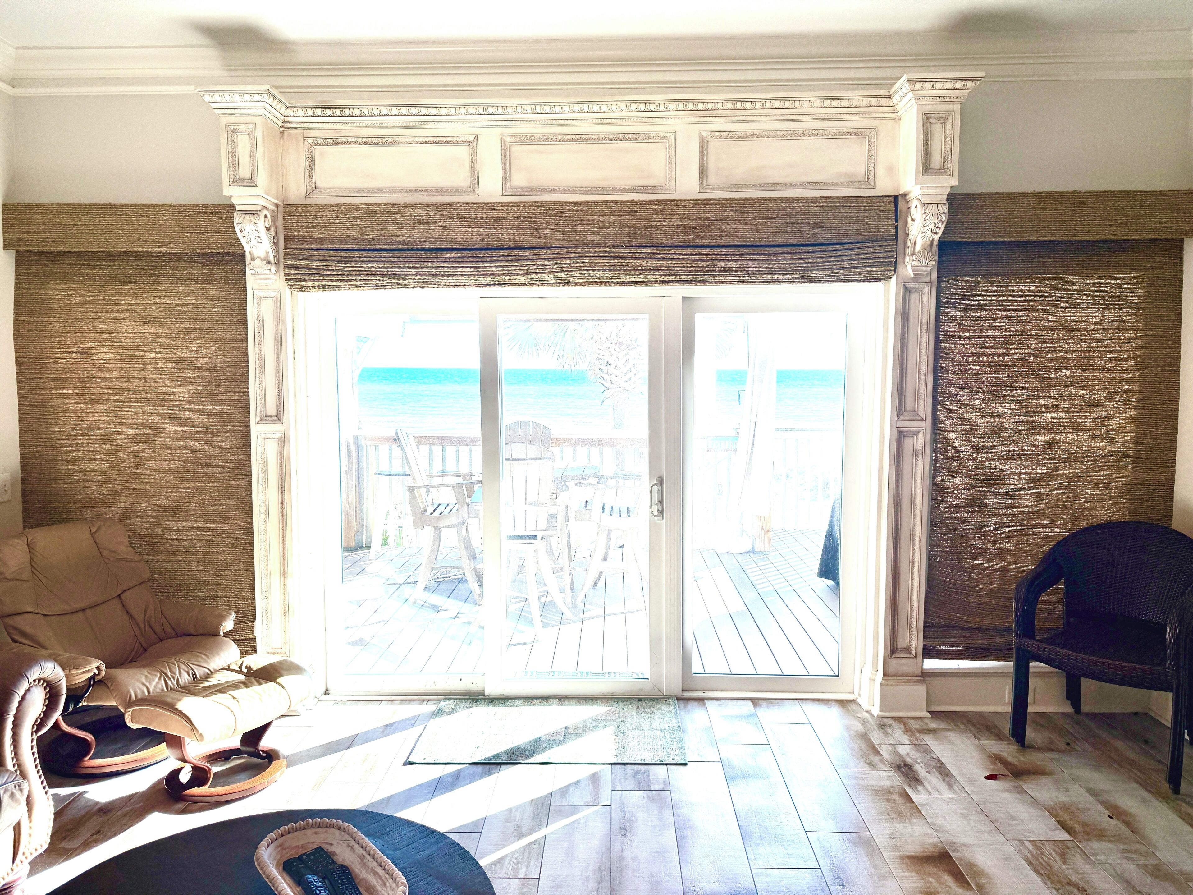 Een kamer met uitzicht op het strand, een houten vloer, een beige bank en een rieten stoel.