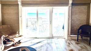 Quarto com vista para a praia, piso de madeira, sofá bege e cadeira de vime.
