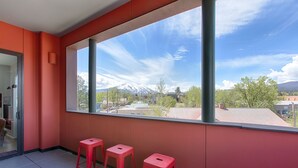 Een balkon met drie rode krukken, een glazen deur en uitzicht op een bergketen.