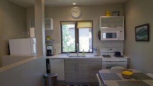 Une cuisine compacte équipée d’un four à micro-ondes, d’une cuisinière et d’un évier. Il y a une horloge au mur et une fenêtre avec des stores.