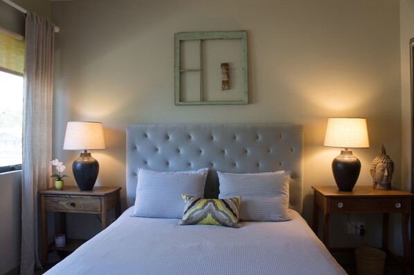A neatly made bed with a tufted headboard, two bedside tables with lamps, and a decorative wall piece.