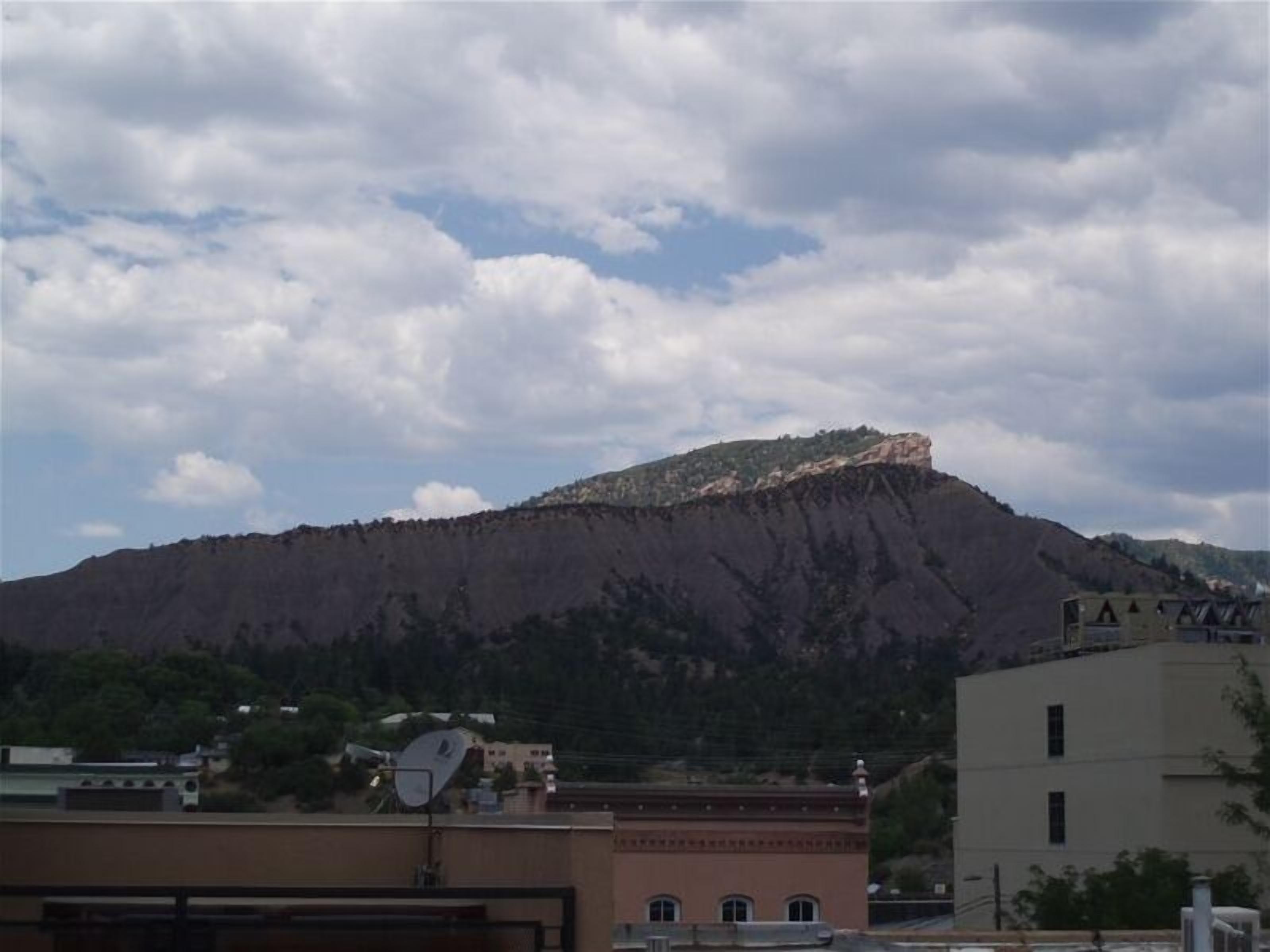 A mountain with a flat top, surrounded by buildings and trees.