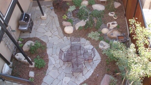 Une cour avec une terrasse en pierre, un espace salon et diverses plantes et rochers.