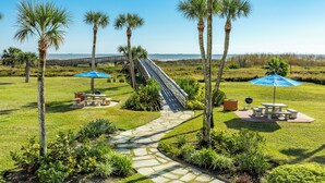 A well-maintained outdoor area with a stone pathway, picnic tables, and umbrellas, overlooking a beach. -   Three bed room, beach- front  end unit with magnificent views, on the11 floor. (Galveston)
