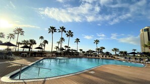 A pool area with lounge chairs and umbrellas, surrounded by palm trees and a clear sky. -   Three bed room, beach- front  end unit with magnificent views, on the11 floor. (Galveston)