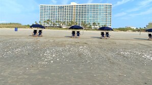 A beachfront hotel with multiple beach umbrellas and lounge chairs. -   Three bed room, beach- front  end unit with magnificent views, on the11 floor. (Galveston)