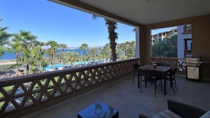A balcony with a view of a pool and palm trees, a table, chairs, and a grill. - Paraiso Del Mar - La Paz Oceanfront 3 Bedroom (La Paz)