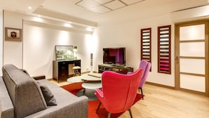 Una sala de estar moderna con un sofá gris, un sillón rojo, un televisor y una mesita.