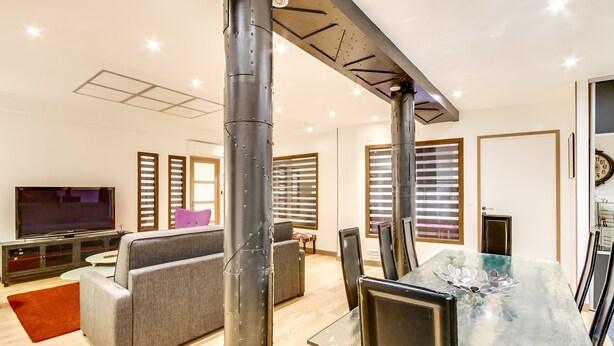 Una sala moderna con sofá, televisor y comedor con sillas y una mesa de vidrio.