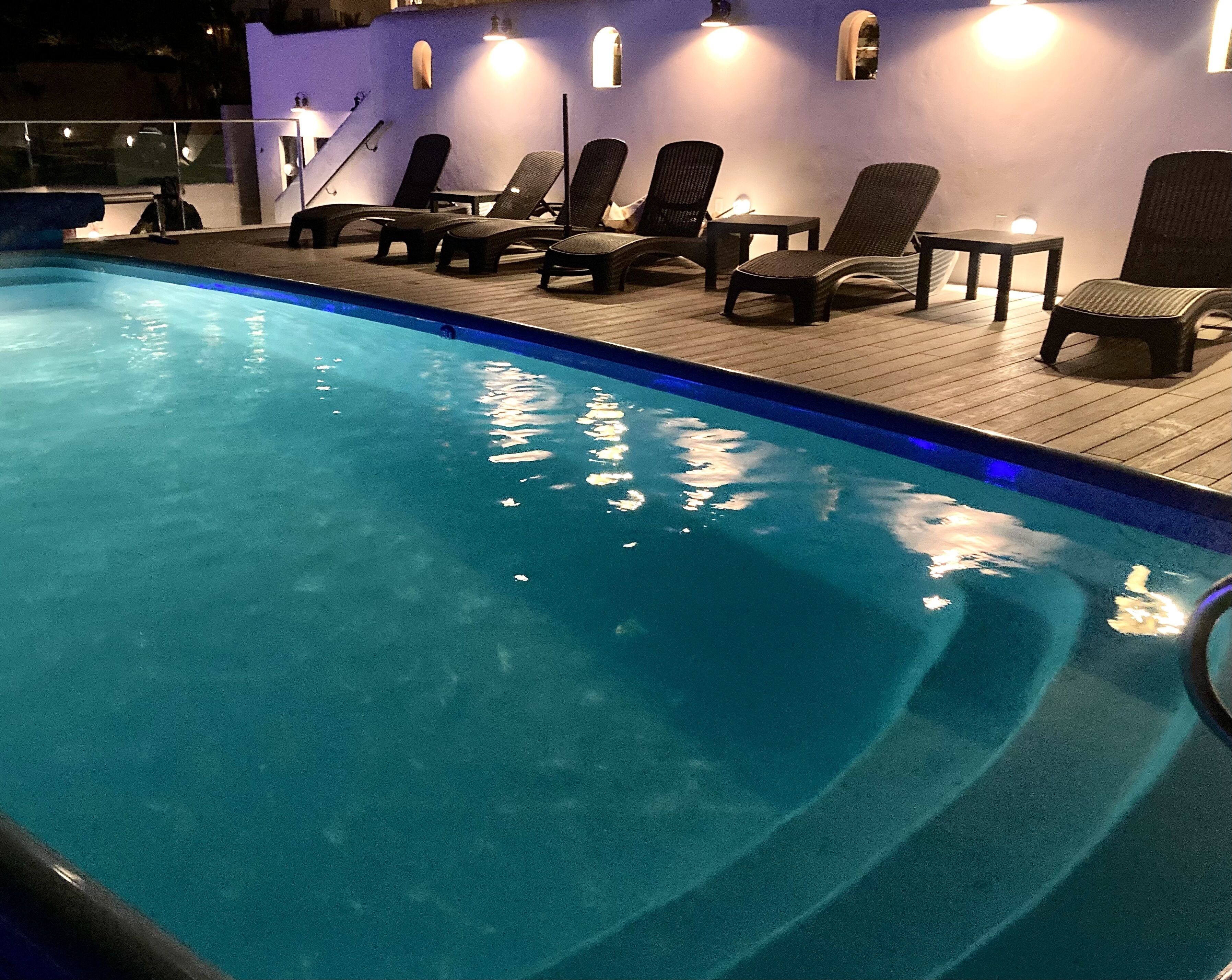 A swimming pool with lounge chairs and tables, surrounded by walls with light fixtures.