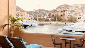 Een balkon met lounge stoelen en een tafel, met uitzicht op een jachthaven met boten en een glooiend stadsbeeld op de achtergrond.