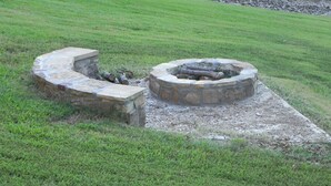 Un hogar de piedra con un banco curvo de piedra, rodeado por un campo cubierto de hierba.