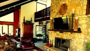 A cozy living room with a stone fireplace, leather sofas, and a staircase leading to an upper level.