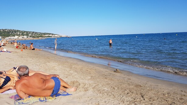 Une plage où des gens se prélassent au soleil et se baignent.