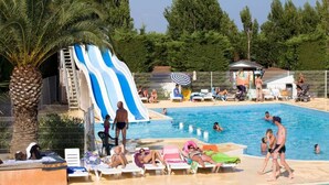 Une piscine avec un toboggan, des palmiers et des gens qui se détendent au bord de la piscine.